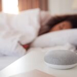 Woman Sleeping In Bed With Voice Assistant On Bedside Table Next To Her